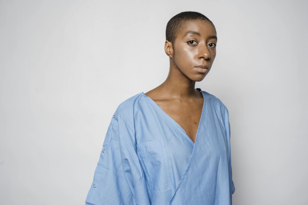 Serious African American female patient with disorder standing against gray background and looking at camera